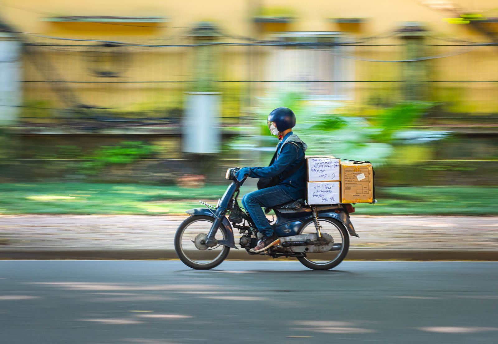 Repartidor en moto con cajas por una calle, con el fondo en movimiento